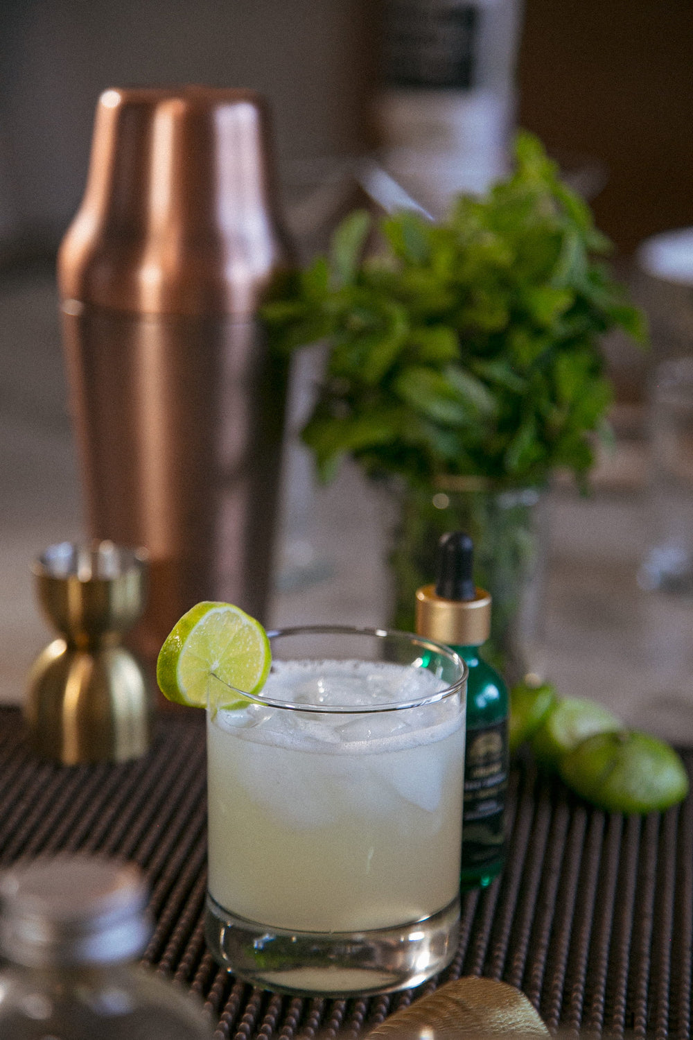 Herbal margarita with lime, fresh mint and Altar Native drops beside a copper shaker